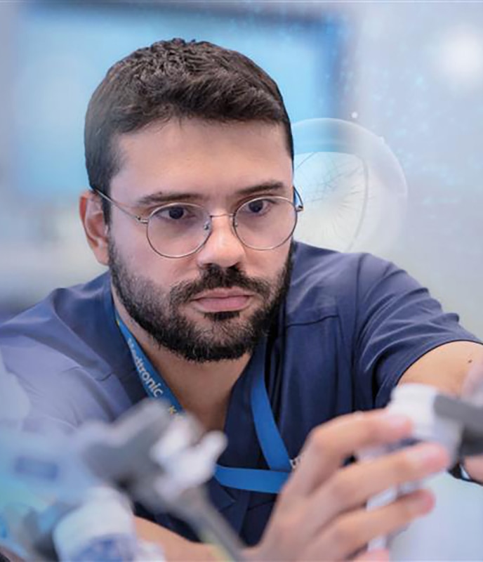 A Medtronic employee wearing a blue top and glasses works in a lab with white and light blue behind him